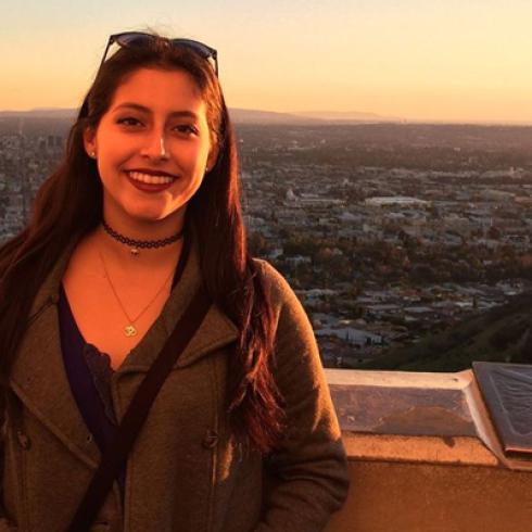 Smiling person at sunset with cityscape in the background. This alt text was added with Al; accuracy may vary.