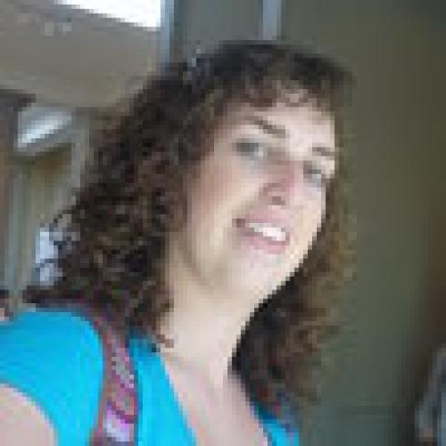 Curly-haired person smiling, wearing a blue shirt indoors. This alt text was added with Al; accuracy may vary.