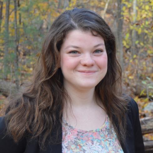 Smiling woman outdoors with autumn foliage in the background. This alt text was added with Al; accuracy may vary.