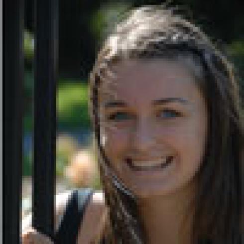 Smiling woman with long brown hair beside a fence in a garden setting. This alt text was added with Al; accuracy may vary.