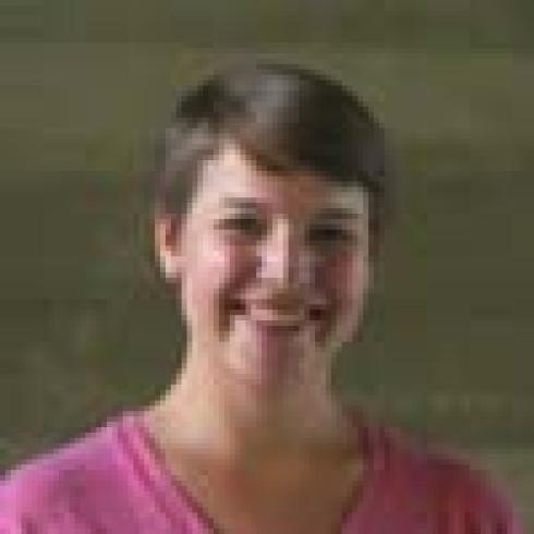 Smiling person with short hair, wearing a pink shirt. This alt text was added with Al; accuracy may vary.