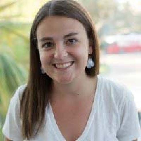 Smiling person with long brown hair in a bright room. This alt text was added with Al; accuracy may vary.
