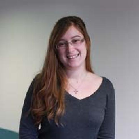 Smiling person with long hair and glasses in gray top. This alt text was added with Al; accuracy may vary.