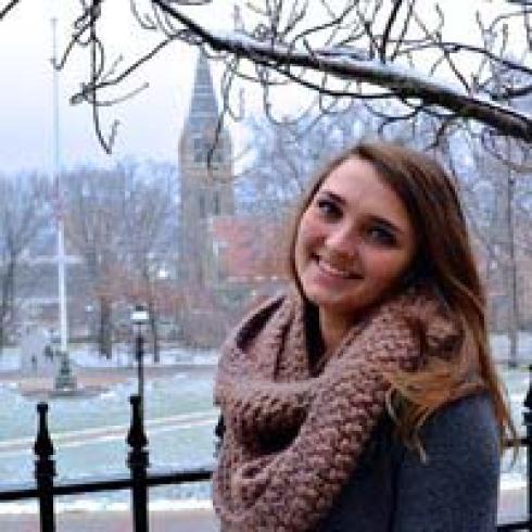 1. Smiling person with long hair by a tree, wearing a knitted sweater.
2. Smiling person with bangs, wearing a striped scarf.
3. Black and white photo of a person laughing at an event.
4. Person in a floral hat and white dress outdoors.
5. Person in a scarf smiling with snowy trees and a church in the background. This alt text was added with Al; accuracy may vary.