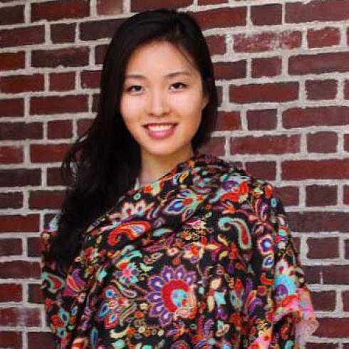 Smiling woman in a colorful shawl stands against a brick wall. This alt text was added with Al; accuracy may vary.