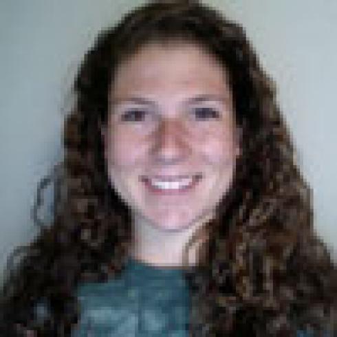 Young woman smiling with long hair, wearing a necklace, against a blurred background. This alt text was added with Al; accuracy may vary.