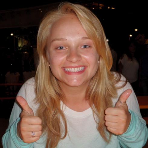 Curly-haired woman smiling in brightly lit interior. This alt text was added with Al; accuracy may vary.
