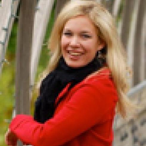 A woman with long hair sitting against a stone wall outdoors. This alt text was added with Al; accuracy may vary.