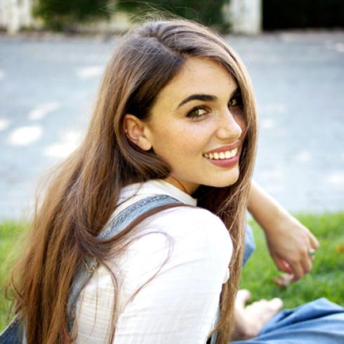 1. Smiling person on a bench in a green park.
2. Young woman with curly hair standing in bright corridor.
3. Man in white jacket, smiling against a gray backdrop.
4. Woman on beach, wearing a blue cap, with rock formations.
5. Woman smiling, sitting on grass, turning back. This alt text was added with Al; accuracy may vary.