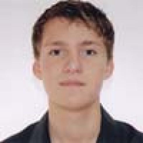 Young person with short hair and neutral expression, wearing a dark shirt. This alt text was added with Al; accuracy may vary.