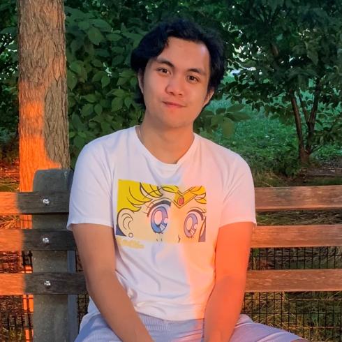 Avery Trinidad sitting on a bench outside in front of some trees. 