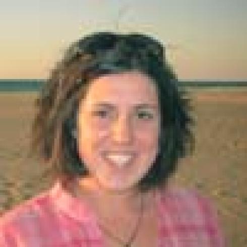 A person in a blue jacket salutes with an indoor background. This alt text was added with Al; accuracy may vary.