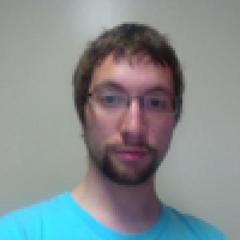 Man with glasses and a beard in a turquoise shirt, neutral expression. This alt text was added with Al; accuracy may vary.