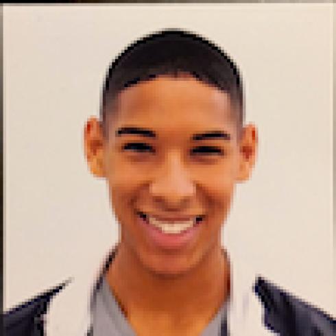 Smiling person in a black and white jacket against a plain background. This alt text was added with Al; accuracy may vary.