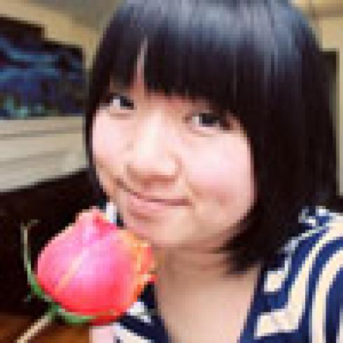 Smiling person holding a pink rose, indoors, wearing a striped shirt. This alt text was added with Al; accuracy may vary.