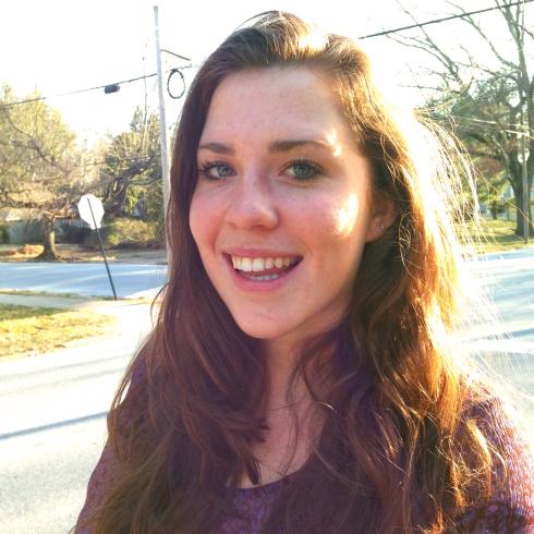 Smiling woman with long hair outdoors, wearing a purple sweater. This alt text was added with Al; accuracy may vary.