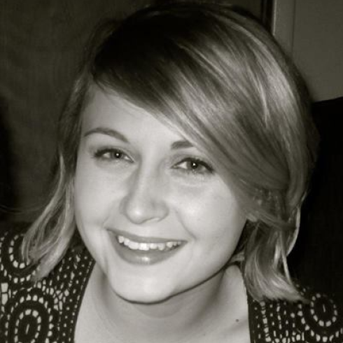 Smiling person holding a peach-colored rose near their face. This alt text was added with Al; accuracy may vary.