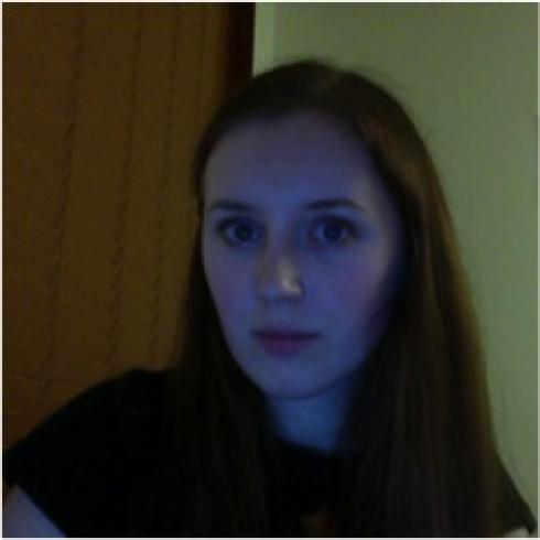 Smiling woman with long hair in a peach top, posters in the background. This alt text was added with Al; accuracy may vary.