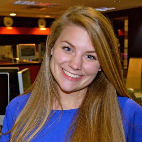 Smiling person holding a large autumn leaf outdoors. This alt text was added with Al; accuracy may vary.