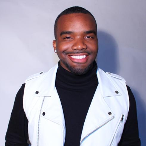 Smiling man in white vest against gray background. This alt text was added with Al; accuracy may vary.