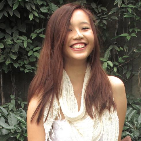 Smiling woman in white dress and scarf, holding a book outside, leafy background. This alt text was added with Al; accuracy may vary.