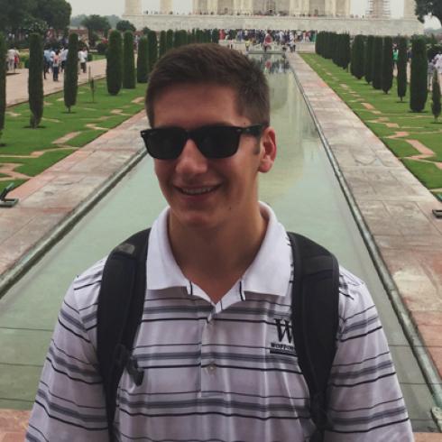 Sunglasses-wearing person smiling in front of symmetrical gardens and a reflective pool. This alt text was added with Al; accuracy may vary.