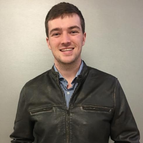 Person wearing a black jacket and smiling against a plain grey background