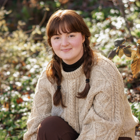 Anja Caverley-Light smiling while sitting in a field of grass and flowers.