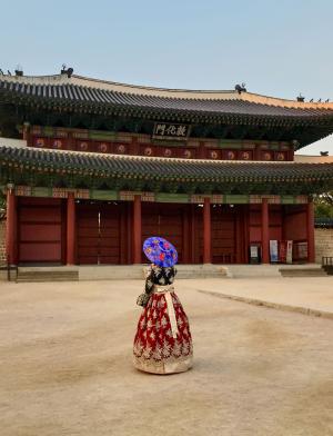 a student poses for a photo at Changdeokgung Palace in Seoul in a traditional Korean hanbok dress and umbrella
