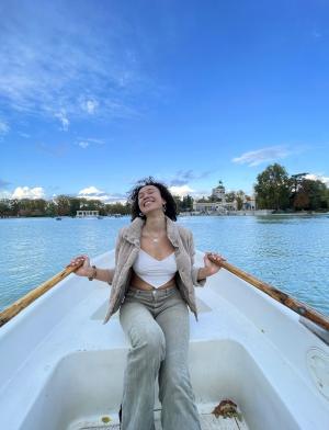 A student is smiling in a white boat in Madrid, Spain as she paddles with two oars.