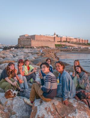 a group of students sitting near the beach with Rabat city in the background