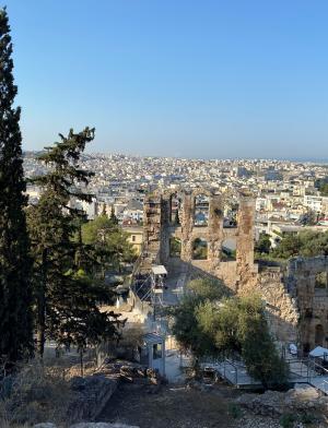 View of Acropolis ruins with cypress trees and cityscape in the background. This alt text was added with Al; accuracy may vary.