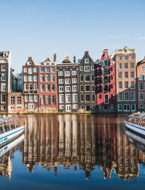 Boats sit in Amsterdam Centraal Canal in front of traditional Amsterdam architecture