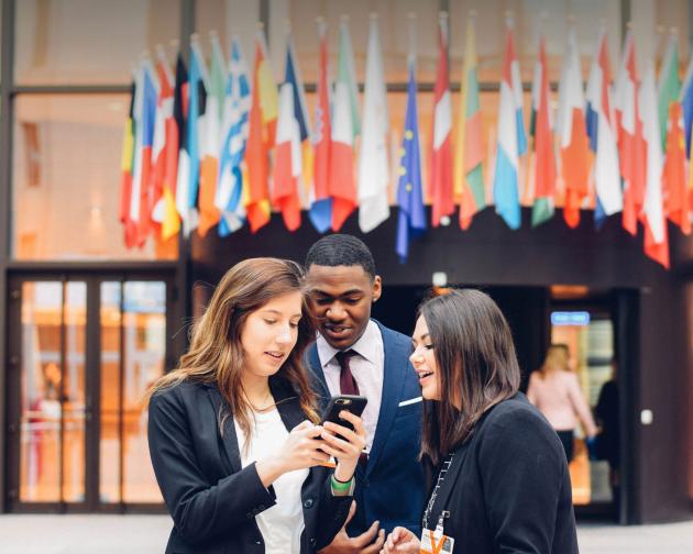 students checking their phone in front of the European Council