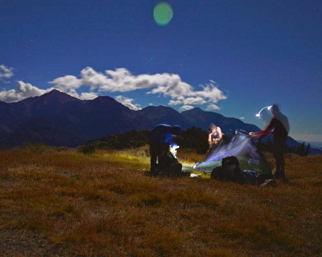 Students set up a tent in New Zealand at night.