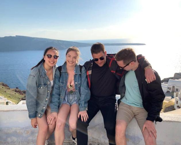 four friends pose for a photo in front of the ocean