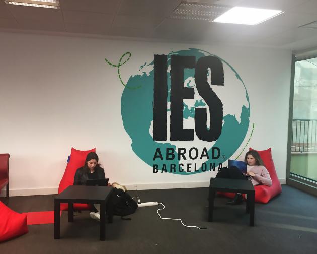 Two students sit in red lounge chairs in the Barcelona Center. Between them in a globe painted on the wall.