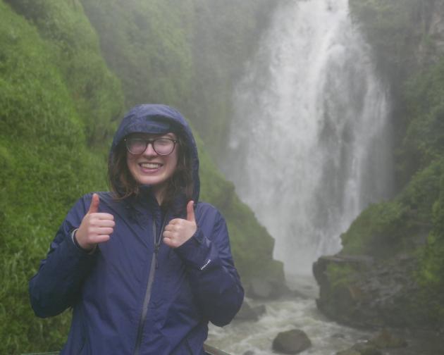 A student gives a thumbs-up in front of a waterfall in Quito, Ecuador.