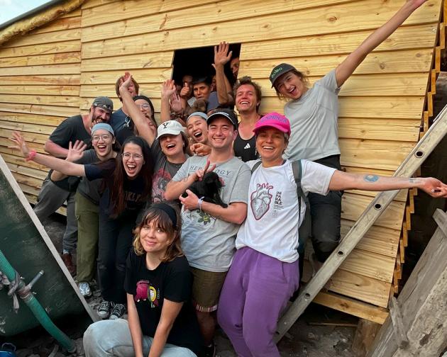 a group of students pose for a photo with a transitional home they built for a family in need