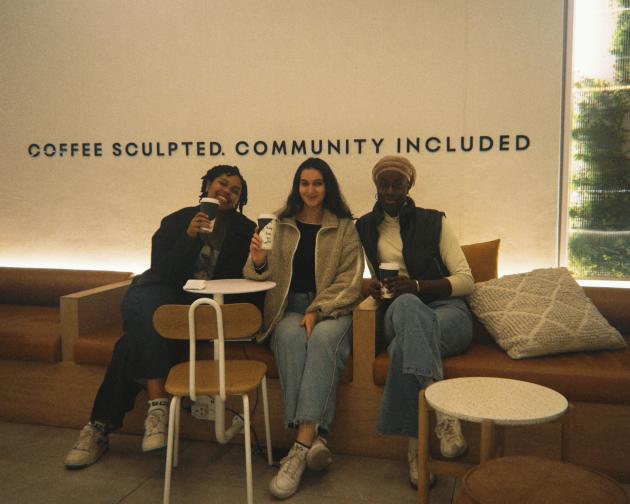 Three people sitting next to each other holding paper cups of chai