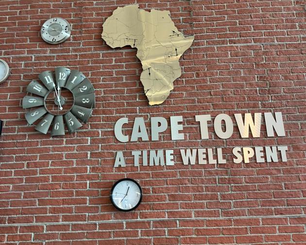 An image showing a wall with a clock in the shape of Africa and text that says "Cape Town A time Well Spend"
