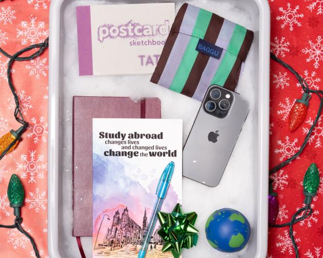 A TSA bin filled with fake snow and items for the "The Book Obsessed" including a sketchbook, notebook, journal, reusable tote, and phone