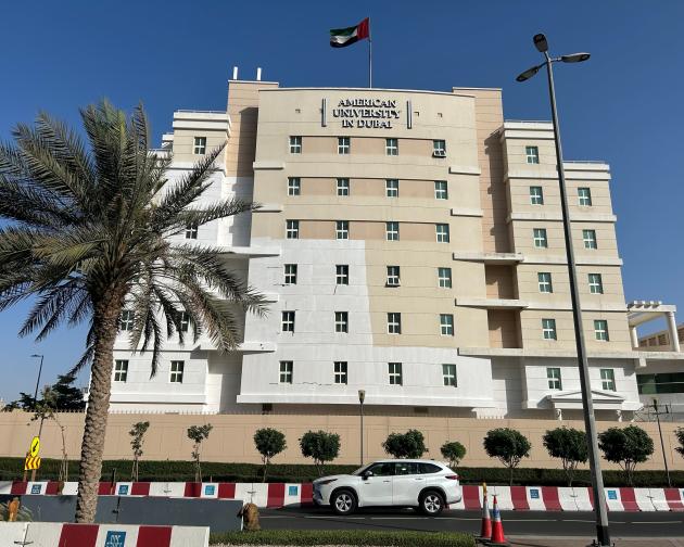 American University of Dubai building with a palm tree and car in front, under a clear blue sky.