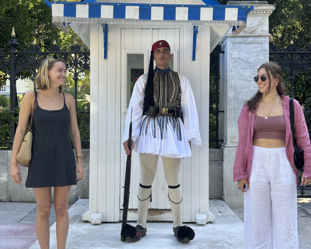 Two students siling and posing with a guard in Athens