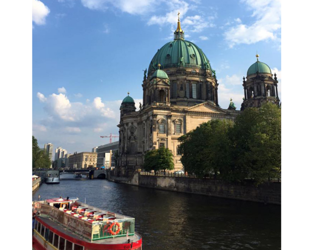 The Berliner Dom with its green dome beside the Spree River, with a boat in the foreground and a blue sky above.