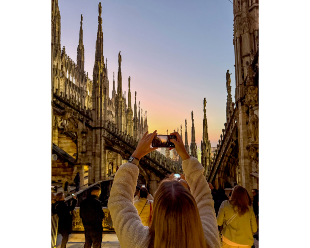 Girl taking a photo at sunset on the rooftop of the Duomo in Milan, surrounded by intricate Gothic spires.