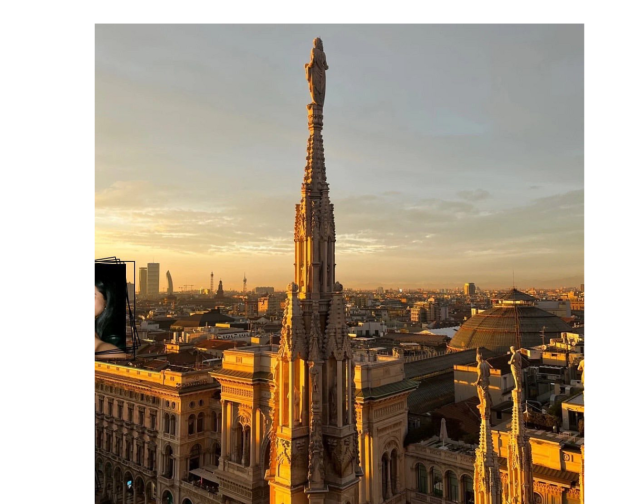 Golden sunset view from the top of the Duomo in Milan, with detailed stone spires glowing in the golden light and the city skyline in the background