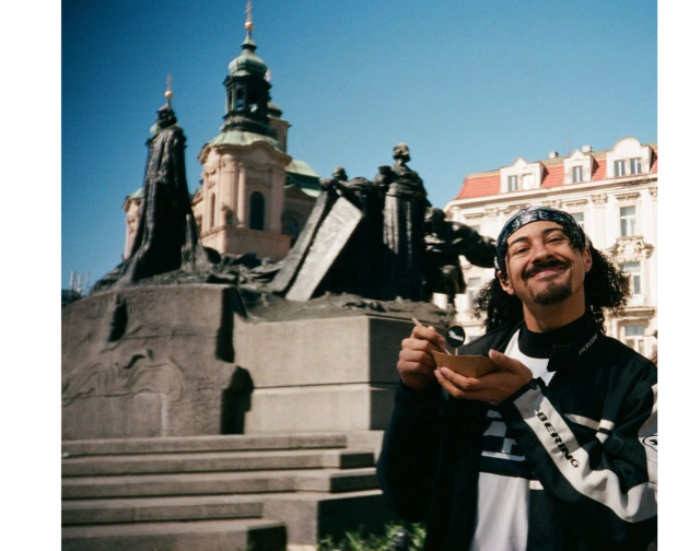 A boy holding a small bowl in front of a historic statue and church towers in berlin on a sunny day.
