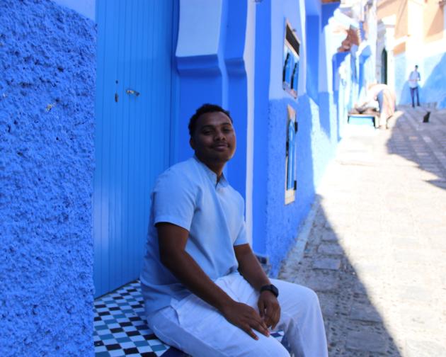 Student posing in front of blue wall in an alleyway filled with blue buildings in Chefchaouen, Morocco