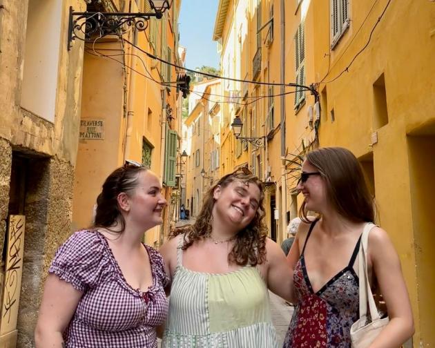 Three friends smiling and laughing in an alleyway in Menton, France on vacation